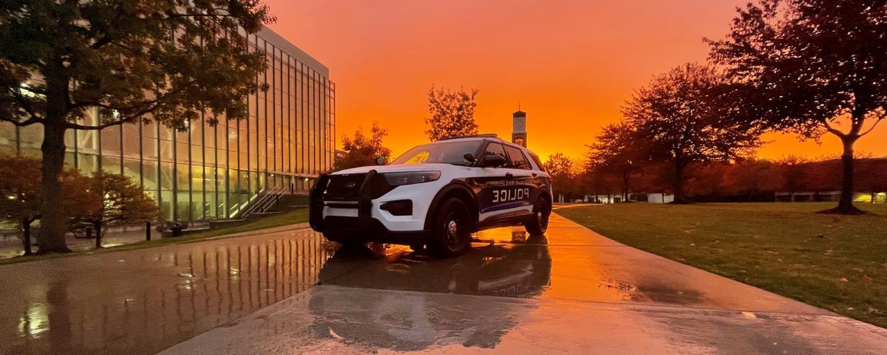 Police cruiser with sunset as background in front of clock tower and library on a rainy day